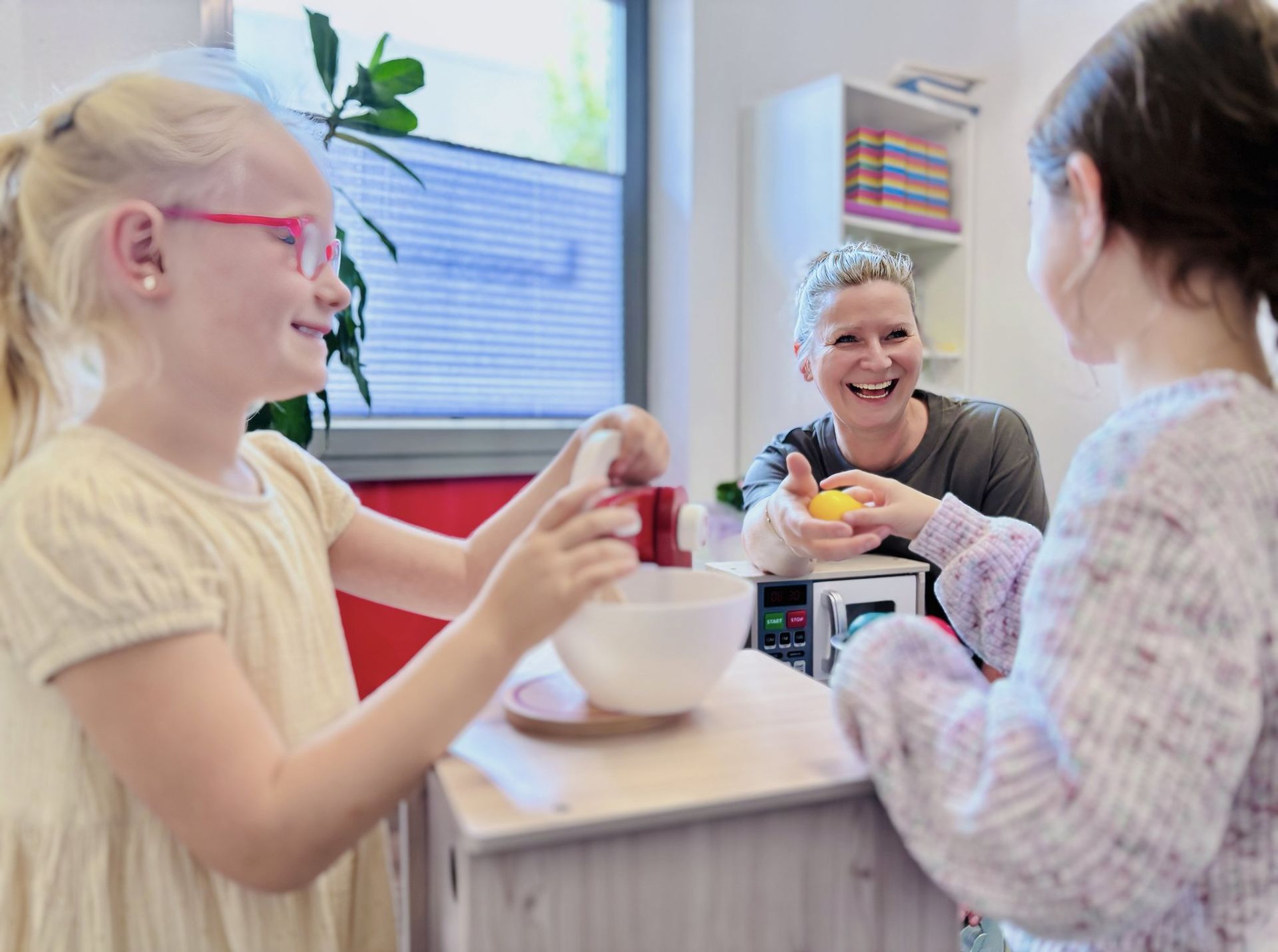 Zwei Kinder im Rollenspiel mit der Logopädin an der Spielküche