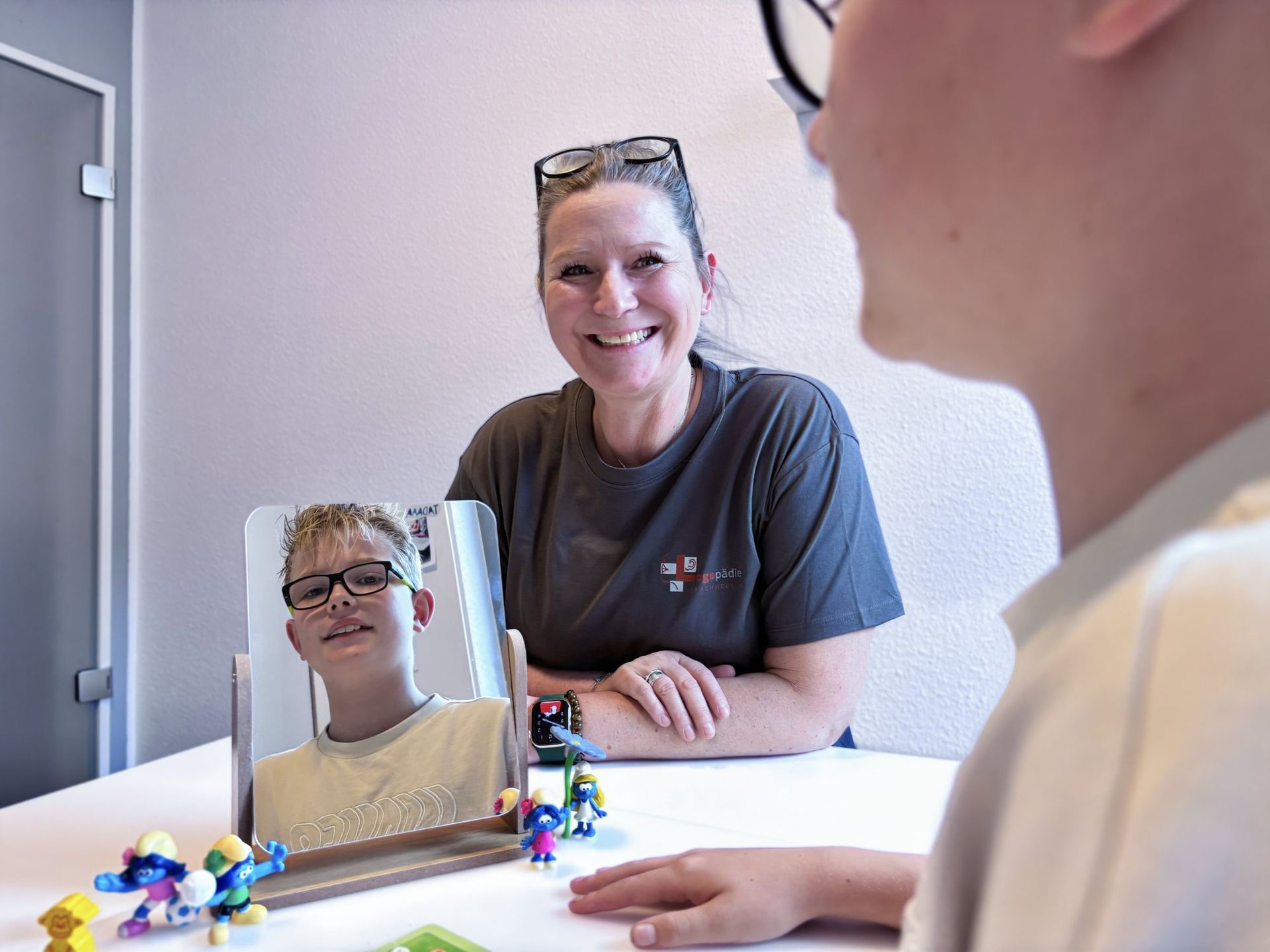 Therapiesitzung am Spiegel: Logopädin übt mit einem Jungen die Aussprache