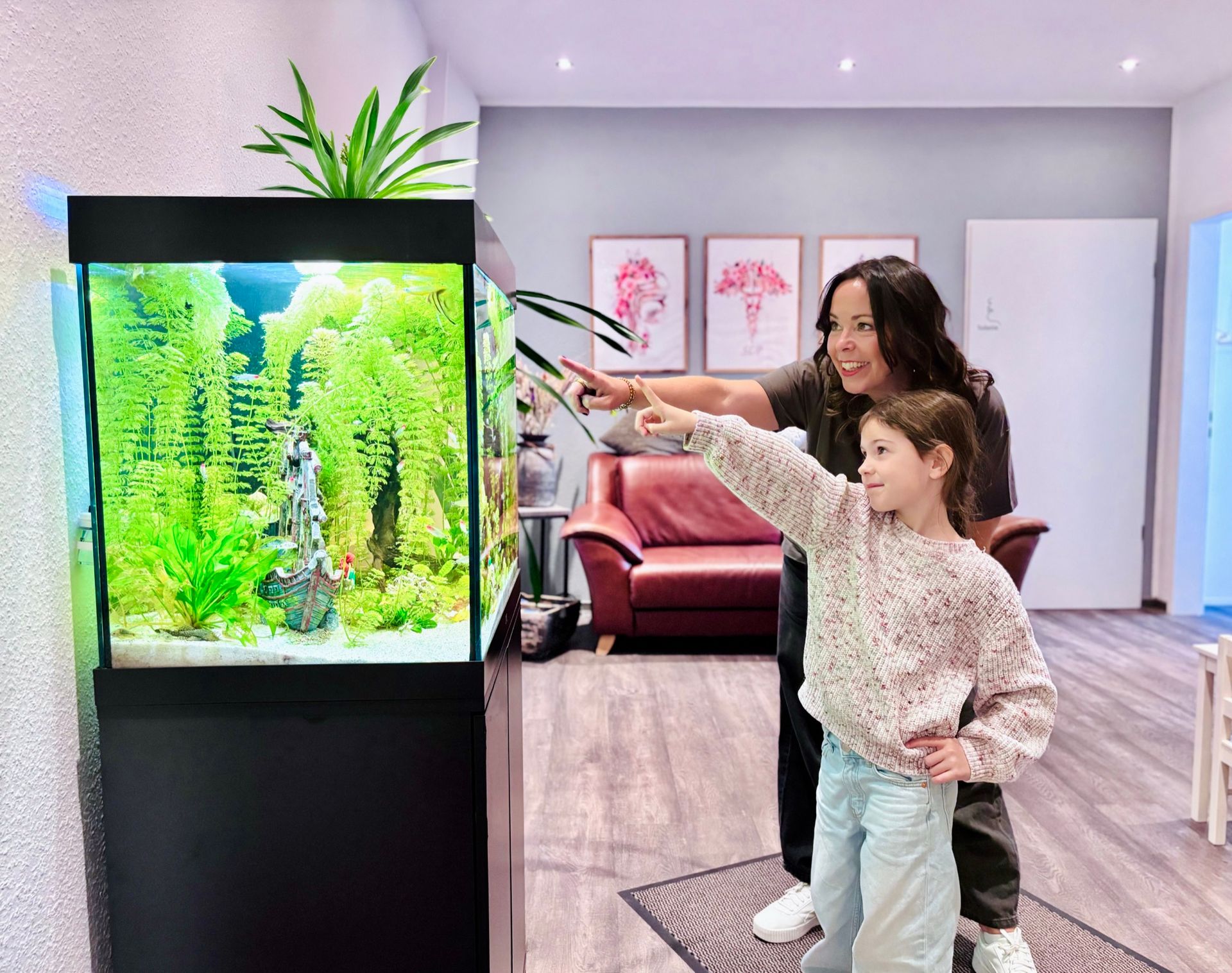 Logopädin und ein Mädchen zeigen gemeinsam auf die Fische im Aquarium des Wartebereichs